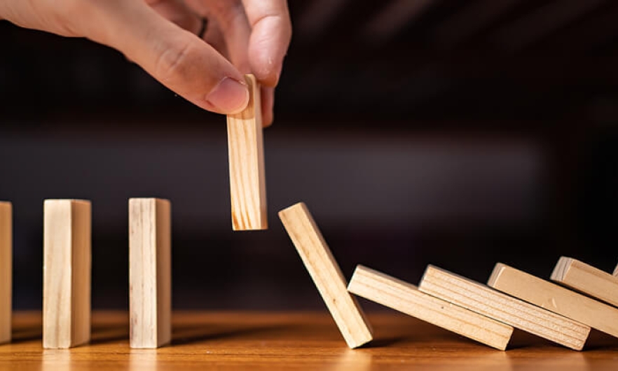 a hand picking up a domino as other dominos fall behind it