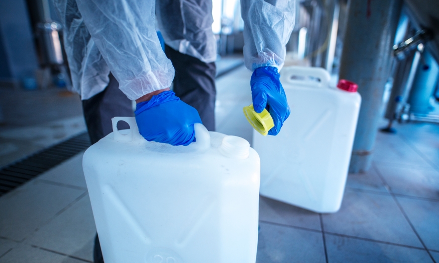 worker in protective clothing and gloves carrying two containers with chemicals