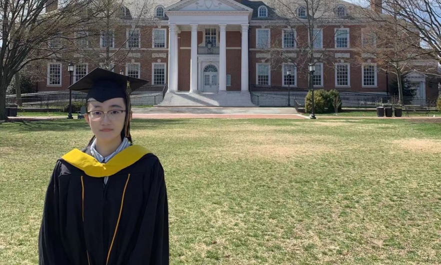 Young woman in cap and gown in front of a university building