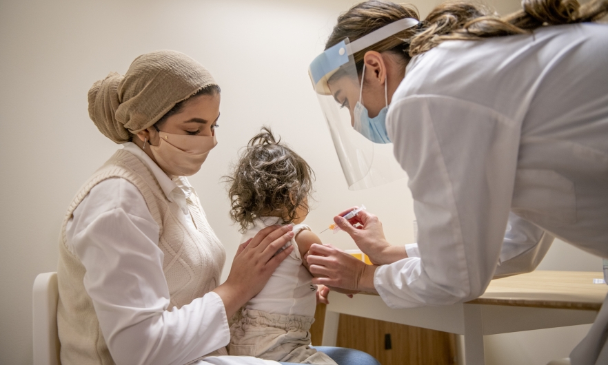 Mother holding child on her lap while she receives vaccine