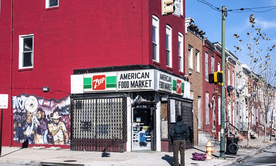 Man standing in front of typical corner shop in East Baltimore