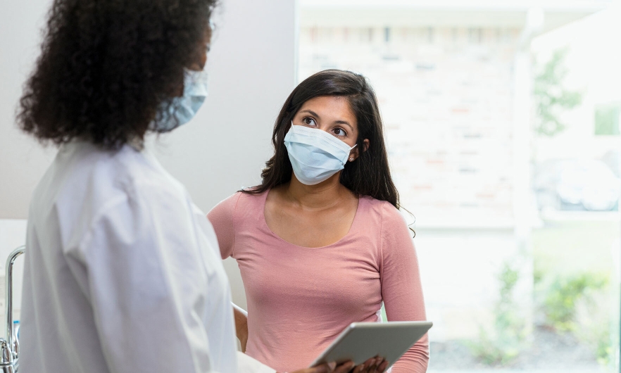 A female patient listening to a female doctor, who is showing her information on a digital tablet