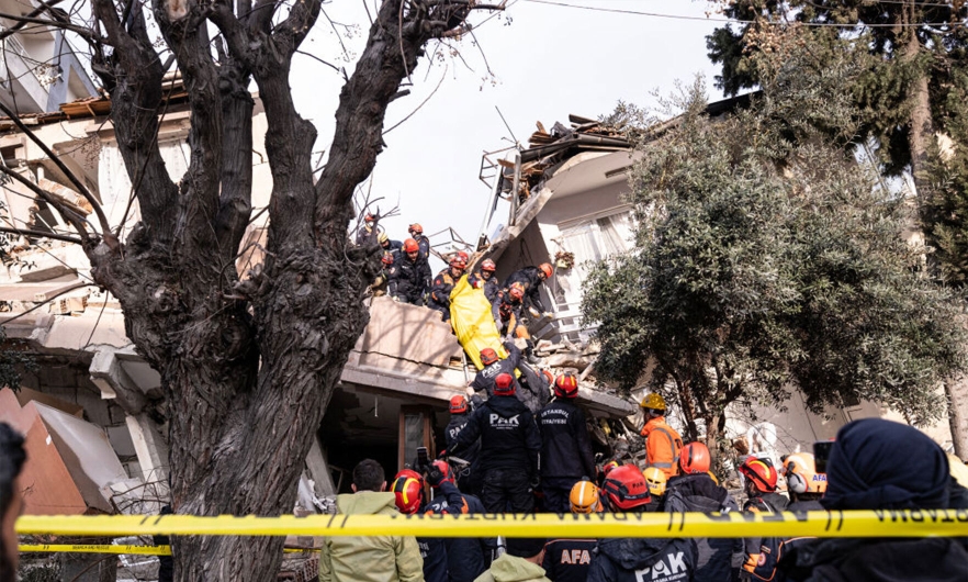 Istanbul first responders standing on top of a wrecked house and rubble handing off a deceased person in a body bag to other first responders on the ground