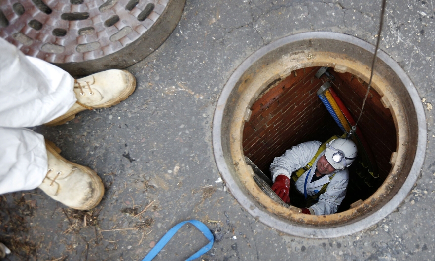 Open sewer in the middle of the street with worker climbing up while another supervises