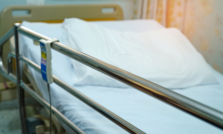 an unoccupied hospital bed with a white sheet; the side guard rail us up