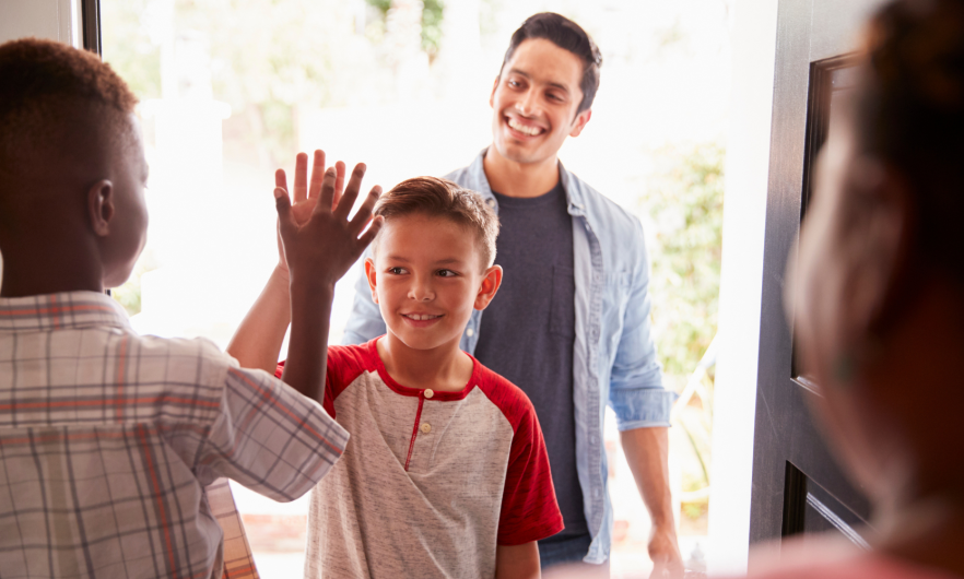 Two children high fiving at the entrance of a house with a father dropping them off