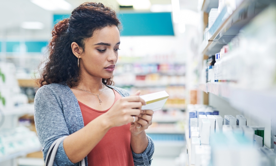 Photograph of a young woman reading the label on a box of medicine in a pharmacy.