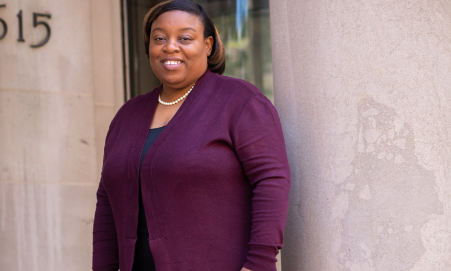 Tanjala S. Purnell stands on the steps with her back to a column, wearing a purple cardigan, black pants and shoes