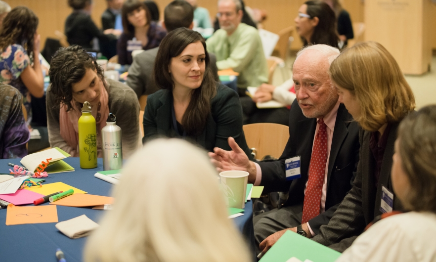 Sid Lerner sits at a round table, with several people listening to him speak. 