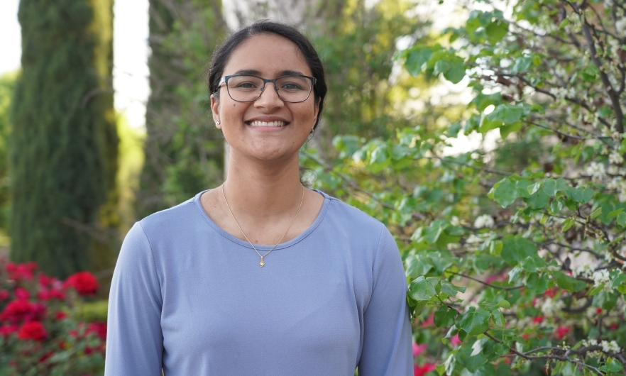 Young woman smiling at camera with rose bushes in background.