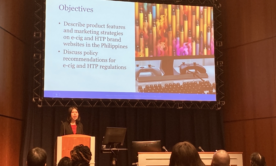 A display screen showing a presentation with a speaker standing at a podium in a meeting room