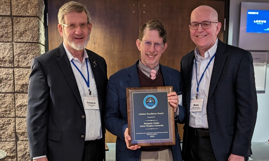 three men posing for a photo, with the center man holding an award