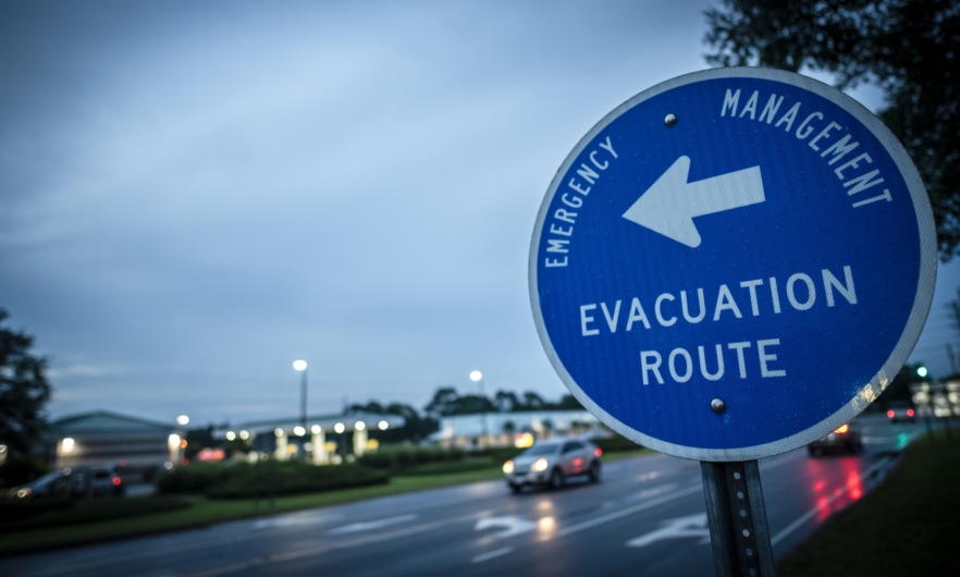 Road sign pointing out evacuation route against gloomy skies