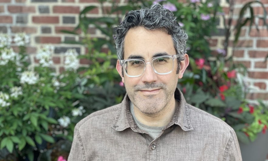 man wearing glasses standing outside with flowers in the background