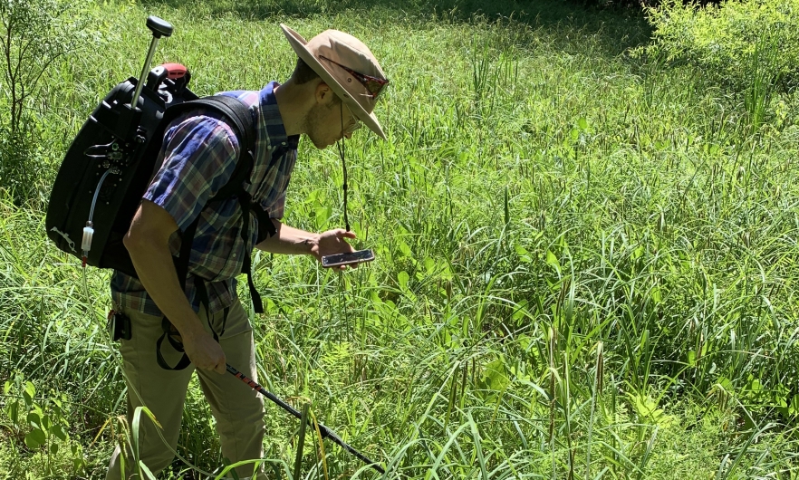 man in a hat with a backpack looking at instrument readings on a phone