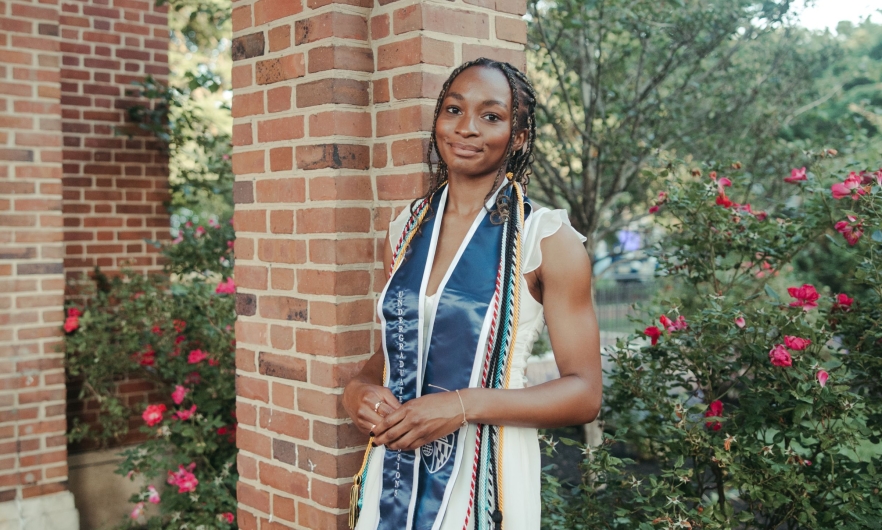 Portrait of student against backdrop of brick columns and flower bushes