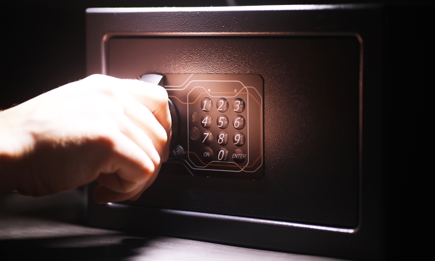 Hand on the handle of a black steel safe with a keypad.