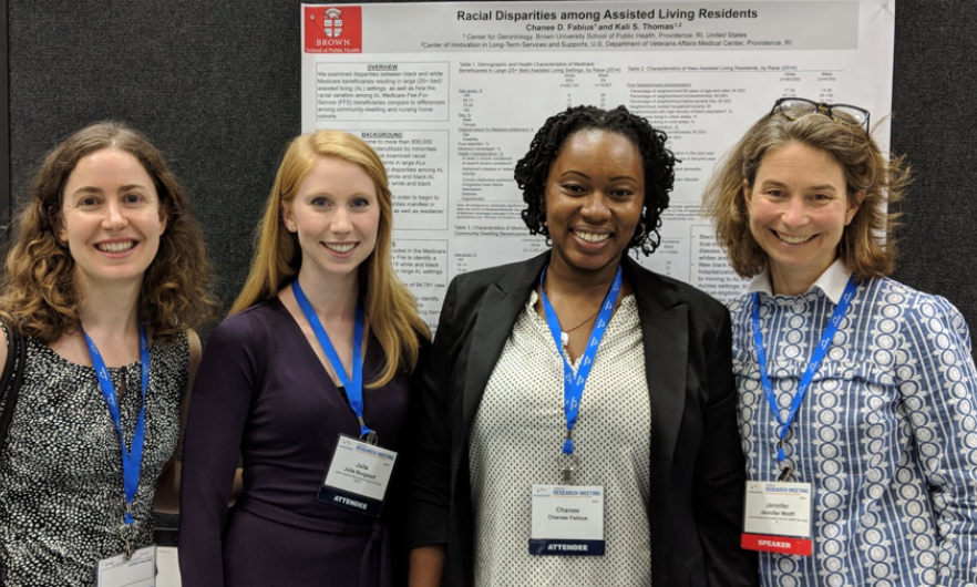 Four women standing side by side in front of presentation poster