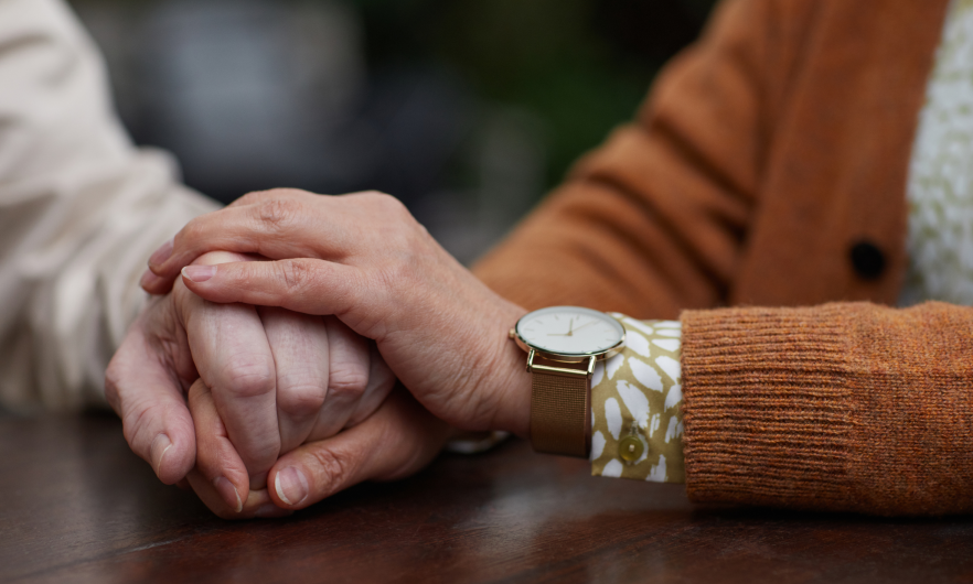 A closeup of two people holding hands at a table. One of the people is younger than the other.