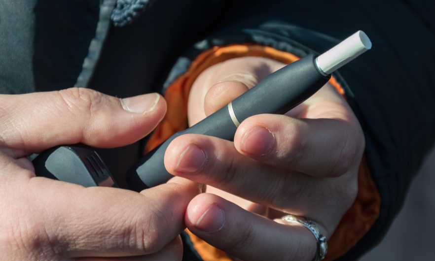 Hands of a man with a light complexion and black winter coat holding a black HTP heated tobacco product