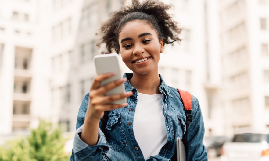 Teenager smiling while holding smartphone outside