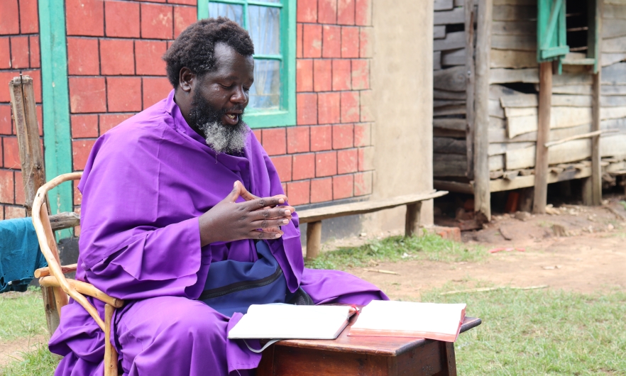  Eliud Wekesa, hands clasped, with a graying beard and wearing a bright purple robe, speaks to visitors outside his home and church compound in Tongaren, Bungoma County, Kenya, on February 29, 2024.