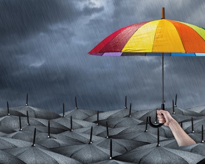 A person holding a colorful umbrella above a sea of black umbrellas in the rain.