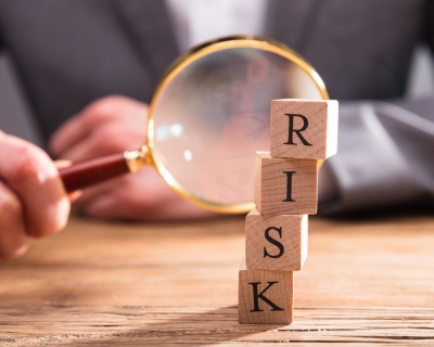 Close-up Of Wooden Blocks With Risk Word In Front Of Person's Hand Holding Magnifying Glass