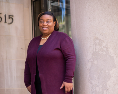 Tanjala S. Purnell stands on the steps with her back to a column, wearing a purple cardigan, black pants and shoes