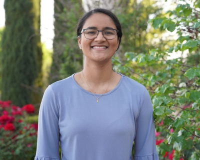 Young woman smiling at camera with rose bushes in background.