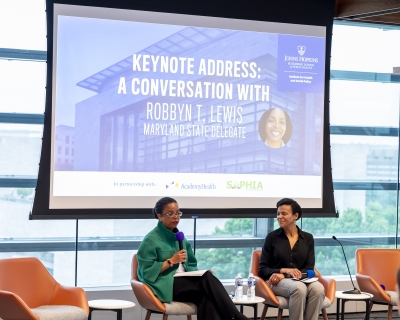 HPM Department Chair Keshia Pollack Porter and Maryland State Delegate Robbyn T. Lewis are seated in front of a projector screen that reads Keynote Address: A Conversation with Robbyn T. Lewis Maryland State Delegate