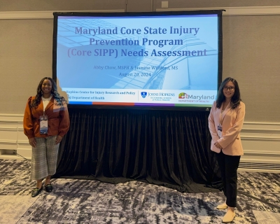 Presenters, Abby Chow and Jasmine Williford standing beside their presentation slide that reads, "Maryland Core State Injury Prevention Program (Core SIPP) Needs Assessment."