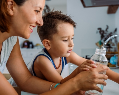 Mother and her toddler filling a glass with filtered water right from the sink's tap.