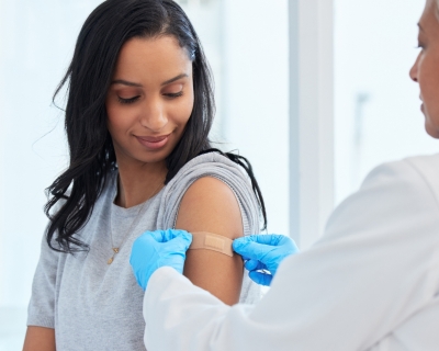 A doctor places a bandaid on a woman's upper arm following vaccination.