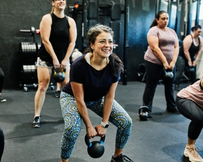 Smiling woman doing kettlebell swings while working out during class in gym
