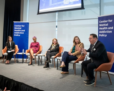 Five adults in business casual attire are seated in a row on stage