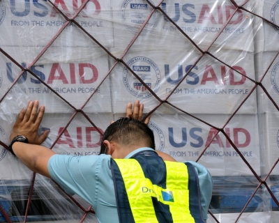 Worker pushes hands against a pallet stacked with boxes of USAID supplies
