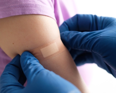 Hands wearing surgical gloves place bandaid on young child's upper arm.