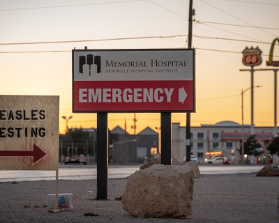 A plywood sign reads "Measles Testing" and points right. Behind it, a larger permanent sign points right towards the Memorial Hospital Emergency Department.
