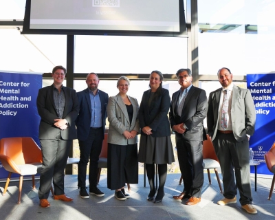 Seven adults wearing business attire stand side by side on stage.