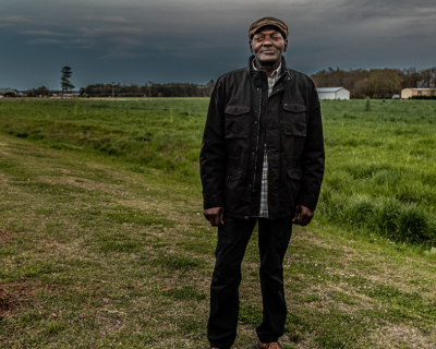 Man standing in front of a field with buildings in the distant background