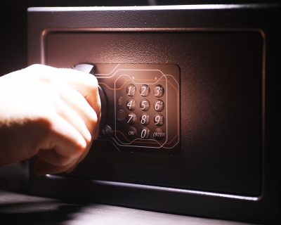 Hand on the handle of a black steel safe with a keypad.