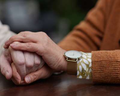 A closeup of two people holding hands at a table. One of the people is younger than the other.