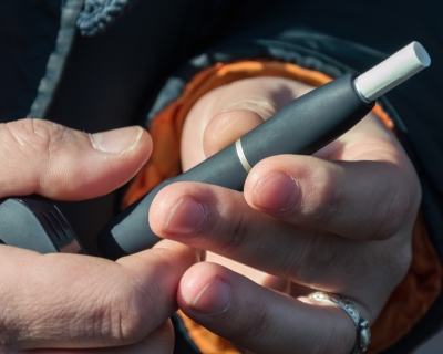 Hands of a man with a light complexion and black winter coat holding a black HTP heated tobacco product