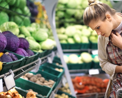 A woman looks at options in a produce section that includes red and green cabbages, onions, tomatoes, and more