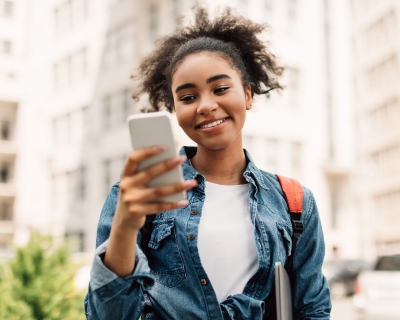 Teenager smiling while holding smartphone outside