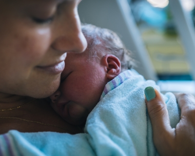 Closeup of mother holding newborn to her chest in hospital bed