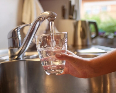 child's hand holding a glass under a running tap