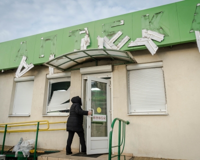 A woman enters a pharmacy after a Russian drone attack on January 31, 2024 in Kharkiv, Ukraine; the letters on the sign (anteka, which means pharmacy in Ukraine) are damaged and falling off the building front.