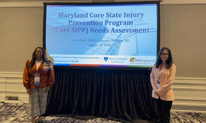 Presenters, Abby Chow and Jasmine Williford standing beside their presentation slide that reads, "Maryland Core State Injury Prevention Program (Core SIPP) Needs Assessment."